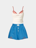 White tank top with red checkered straps and blue shorts on a light gray background